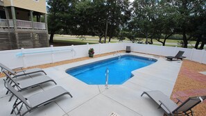 Une piscine rectangulaire dotée d’un plongeoir, entourée d’une clôture blanche et agrémentée de plusieurs chaises longues.