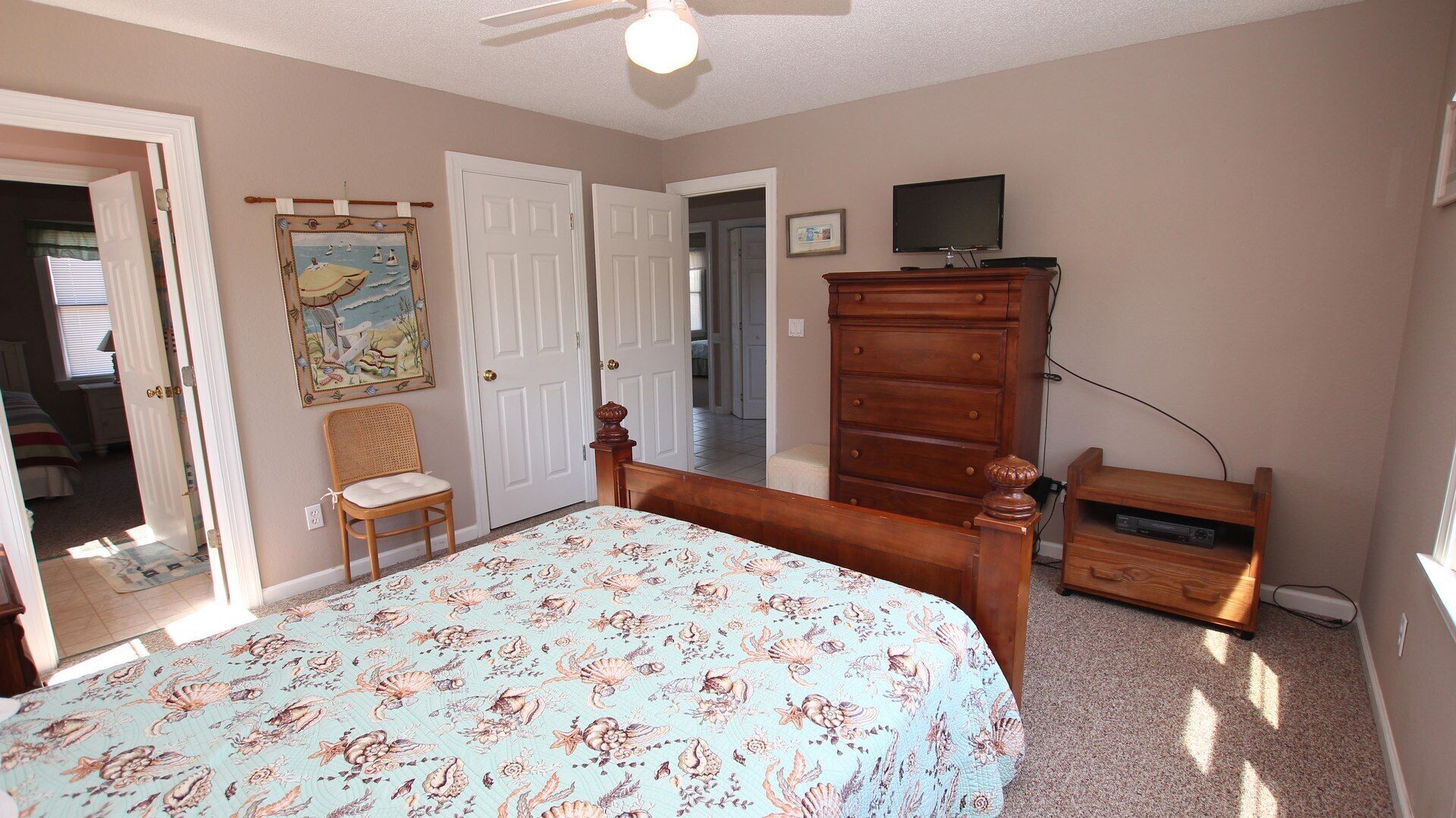 A bedroom with a bed, a dresser, a television, and a door leading to another room.