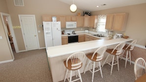 A kitchen with a central island, wooden cabinets, a microwave, a stove, and bar stools.