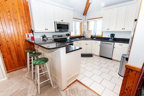 A modern kitchen with white cabinetry, a central island with stools, a built-in microwave, and a coffee maker.