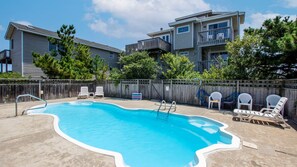 A backyard with a swimming pool, lounge chairs, and a wooden fence.