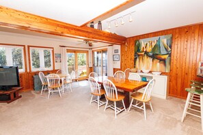 A dining area with a wooden table and chairs, a television, and a painting of sailboats on the wall.
