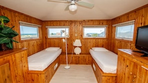 A cabin with two wooden bunk beds, a ceiling fan, a television, and windows with views of the ocean.