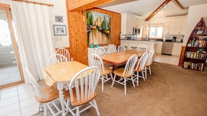 A dining area with a wooden table and white chairs, a kitchen with white cabinets, and a bookshelf filled with books.