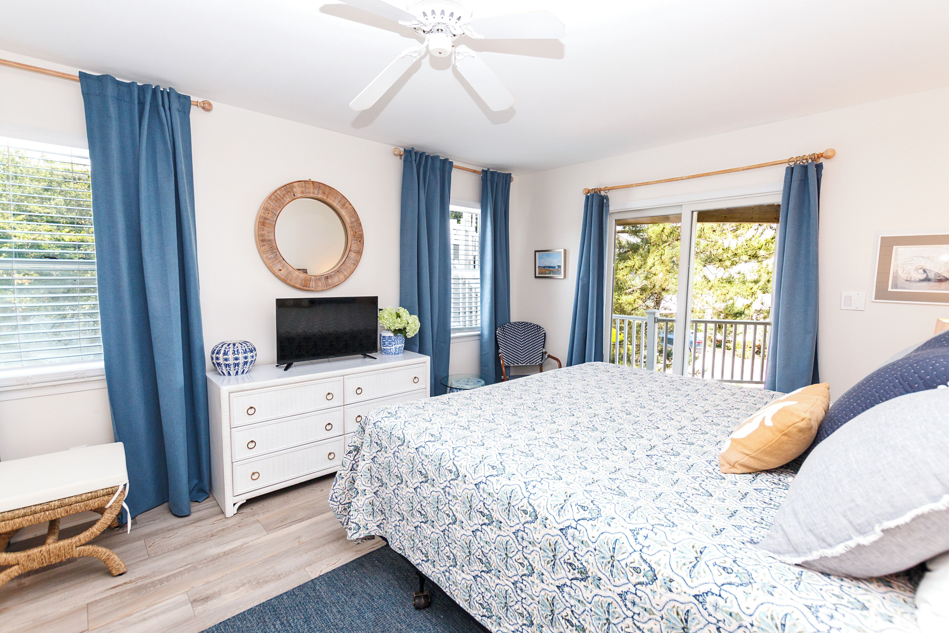 A bedroom with a bed, a dresser, a television, a chair, and a balcony with a view of trees.