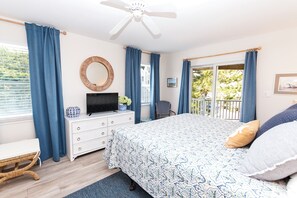 A bedroom with a bed, a dresser, a television, a chair, and a balcony with a view of trees. - Oceanside, Private Pool, Hot Tub, Close to beach access, 224, Its All Good (Corolla)