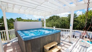 A hot tub under a white pergola with a wooden bench and a pool in the background.