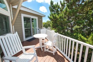 A wooden deck with a white table and chairs, a glass door entrance, and a view of pine trees. - Oceanside, Private Pool, Hot Tub, Close to beach access, 224, Its All Good (Corolla)