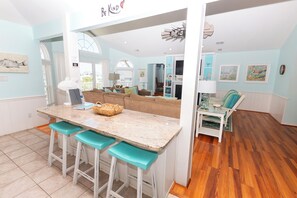 A kitchen with a central island, bar stools, and a view of the living area. - Oceanside, Private Pool, Hot Tub, Close to beach access, 224, Its All Good (Corolla)
