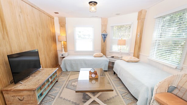A cozy room with a television, two beds, a small table, and a window with blinds.