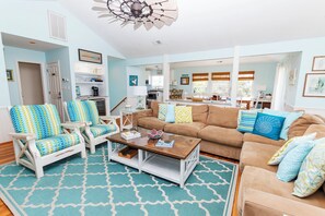 A spacious living room with a large brown sofa, two white armchairs with blue and yellow patterned cushions, a wooden coffee table, and a patterned rug. - Oceanside, Private Pool, Hot Tub, Close to beach access, 224, Its All Good (Corolla)