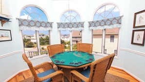 A room with a green felt blackjack table, wicker chairs, and large windows with decorative curtains. - Oceanside, Private Pool, Hot Tub, Close to beach access, 224, Its All Good (Corolla)