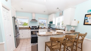 A kitchen with a central island, bar stools, a refrigerator, and a view of the outside.