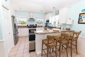 A kitchen with a central island, bar stools, a refrigerator, and a view of the outside. - Oceanside, Private Pool, Hot Tub, Close to beach access, 224, Its All Good (Corolla)