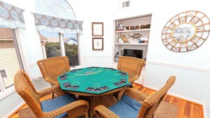 A room with a green felt casino table, wicker chairs with blue cushions, a bookshelf with nautical decorations, and a large mirror with a circular frame. - Oceanside, Private Pool, Hot Tub, Close to beach access, 224, Its All Good (Corolla)