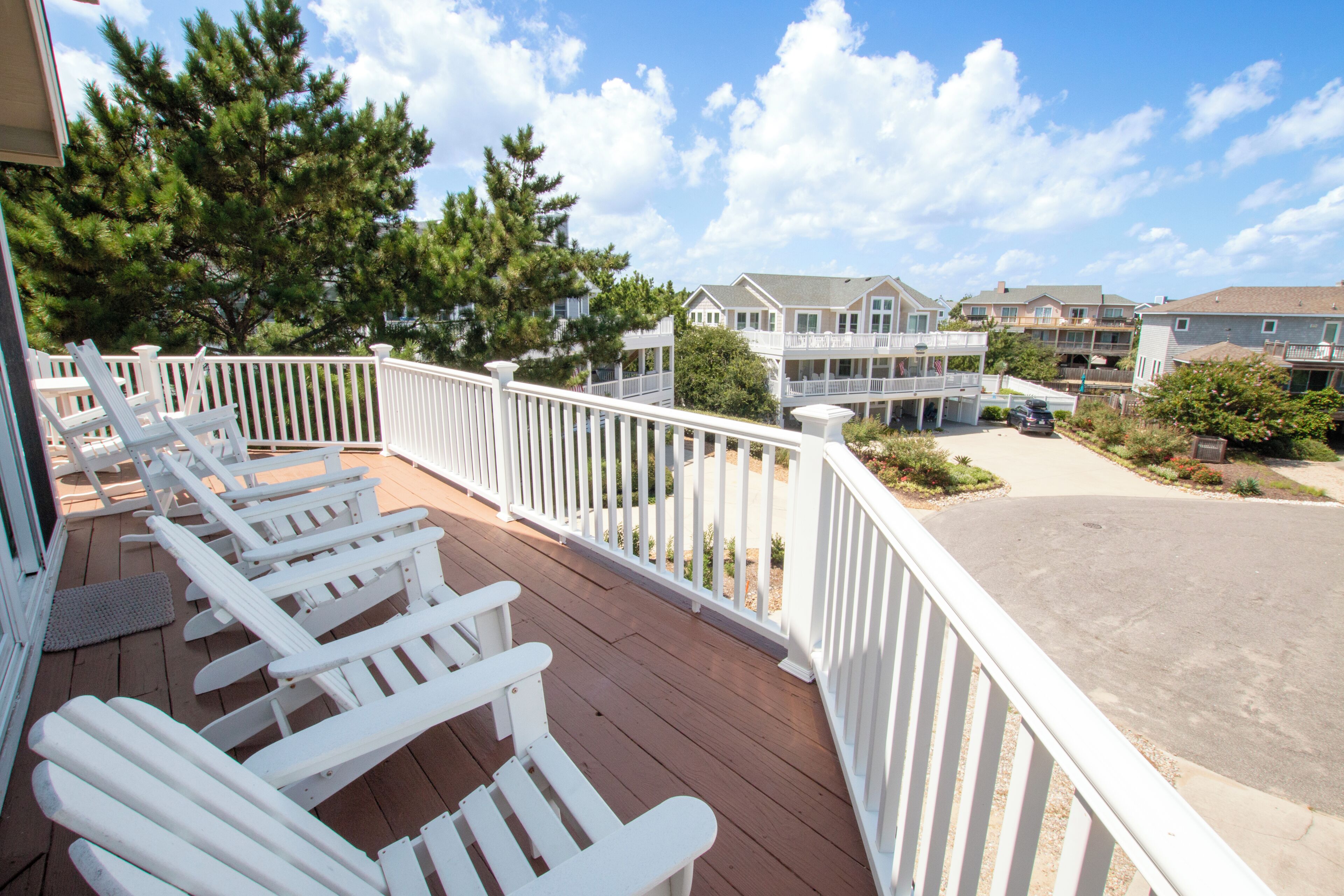 A wooden deck with white railings and several Adirondack chairs.
