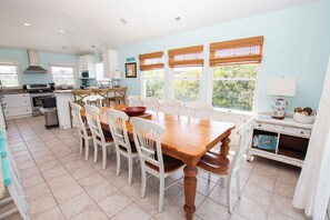 A spacious kitchen with a dining area, featuring a large wooden table and white chairs, a built-in oven, and a window with a view of greenery. - Oceanside, Private Pool, Hot Tub, Close to beach access, 224, Its All Good (Corolla)