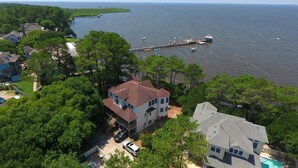 A large house with a two-story structure, a dock extending into a lake, and surrounding lush greenery. - Soundfront, Sound views! Dogs Welcome, Private Pool! 520, Bay Spray (Corolla)