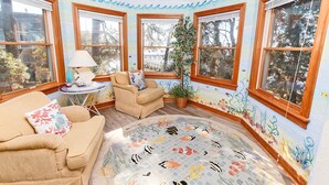 A sunroom with large windows, a beige sofa, a small table with a lamp, and a colorful rug. - Soundfront, Sound views! Dogs Welcome, Private Pool! 520, Bay Spray (Corolla)