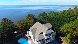 A two-story house with a swimming pool, surrounded by trees and overlooking a large body of water. - Soundfront, Sound views! Private Pool, Community Amenities, 504, Lost N' Sound (Corolla)