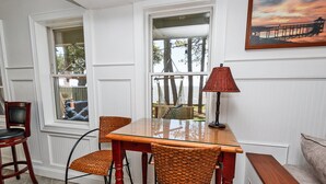 A dining area with a glass-top table, wicker chairs, and a red lamp. - Soundfront, Sound views! Private Pool, Community Amenities, 504, Lost N' Sound (Corolla)
