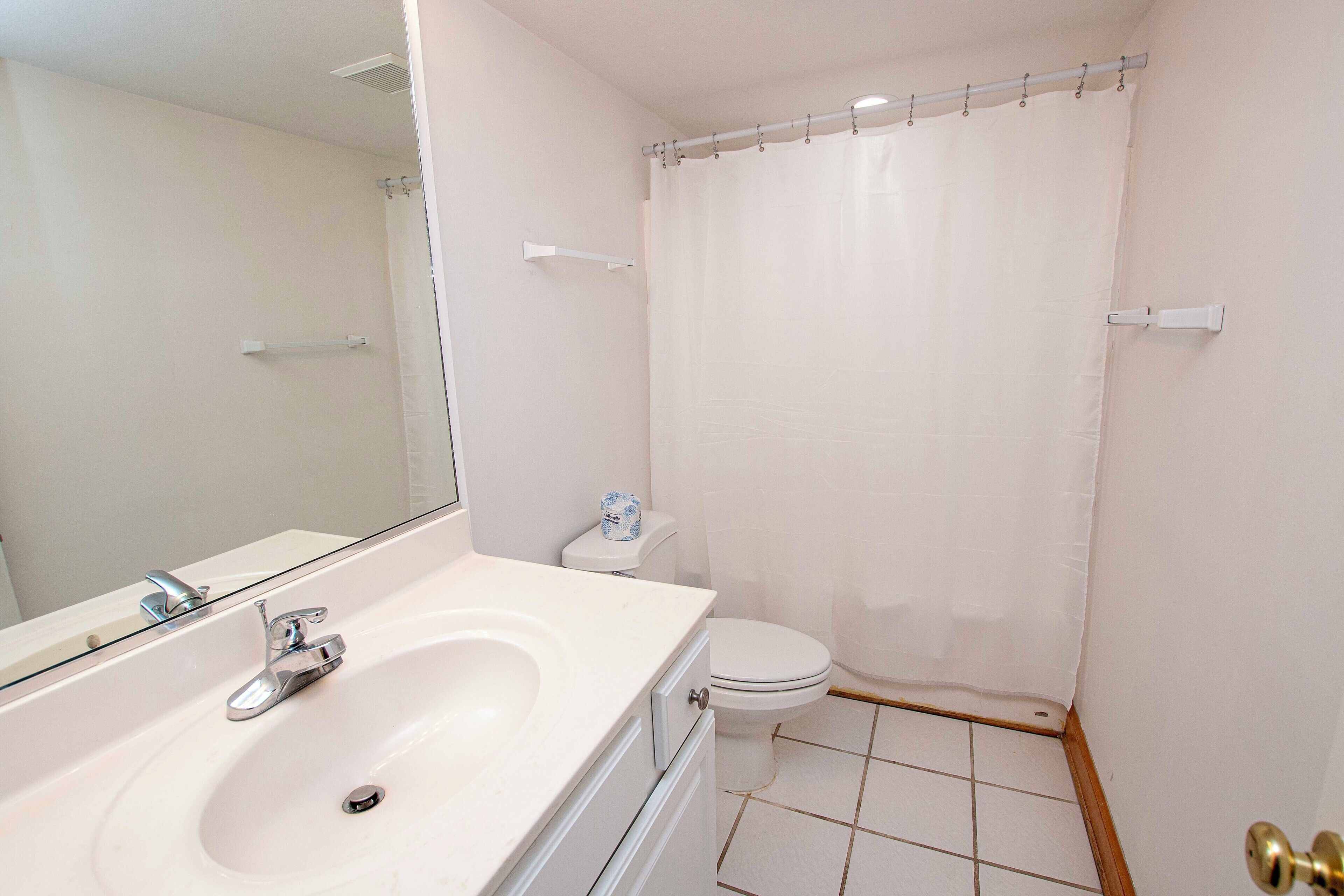 A bathroom with a white sink, a mirror, a toilet, and a shower curtain.