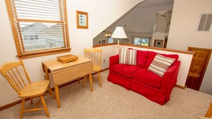 Um quarto aconchegante com um sofá vermelho, cadeiras de madeira, uma pequena mesa de madeira e uma janela com persianas.