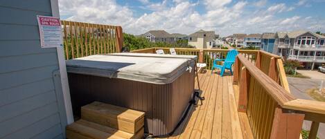 Een houten terras met een jacuzzi, een stoel en een waarschuwingsbord met regels voor het bubbelbad.