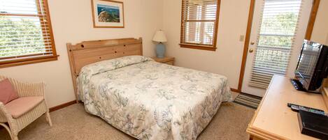 A bedroom with a bed, a chair, a desk with a TV, and a door with blinds.