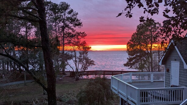 A wooden deck with a staircase leading to a cabin overlooking a sunset over the water. - Semi-Soundfront, Rec Room, Community Amenities, 533,Sound Secret (Corolla)