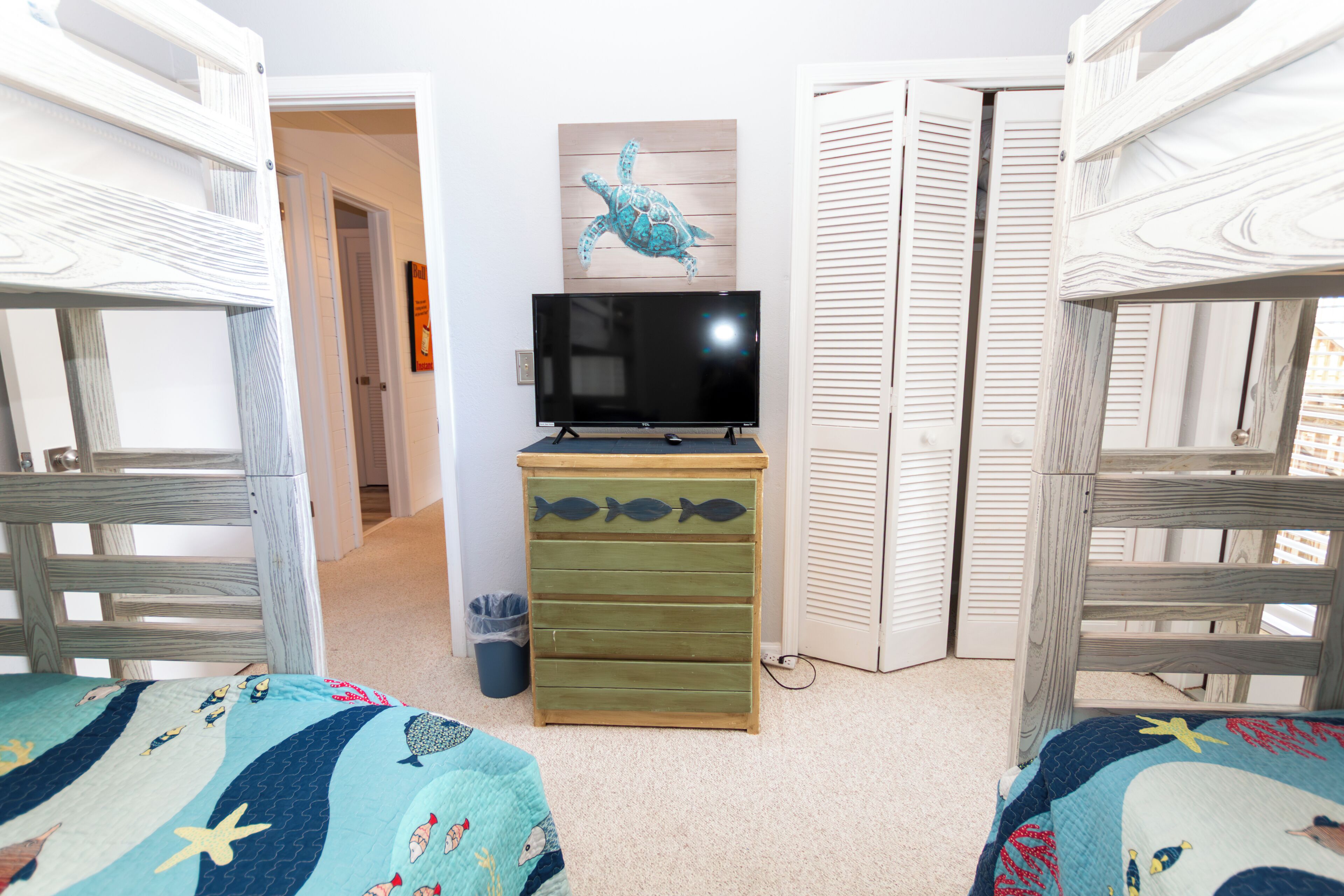 Una habitación con literas, un televisor sobre un soporte de madera y una pared con un caracol pintado.