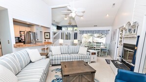 A spacious living room with a large sofa, a coffee table, and a fireplace. There is a kitchen area with a refrigerator and a dining table. - Semi-Soundfront, Rec Room, Community Amenities, 533,Sound Secret (Corolla)