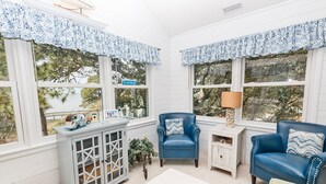 A cozy room with a blue armchair, a white cabinet, and a view of trees through large windows. - Semi-Soundfront, Rec Room, Community Amenities, 533,Sound Secret (Corolla)