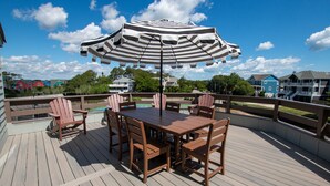 Eine Holzterrasse mit Tisch und Stühlen, einem gestreiften Sonnenschirm und Blick auf Häuser und Bäume.