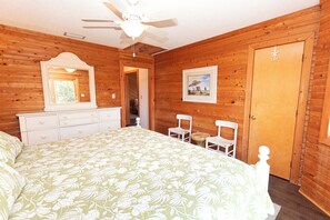 A bedroom with a bed, dresser, chairs, a ceiling fan, a door, and a framed picture on the wall.