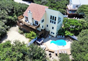 A two-story house with a swimming pool, deck chairs, and a covered patio.
