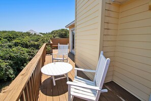 A wooden deck with a round table and two white chairs, overlooking a garden with dense foliage.