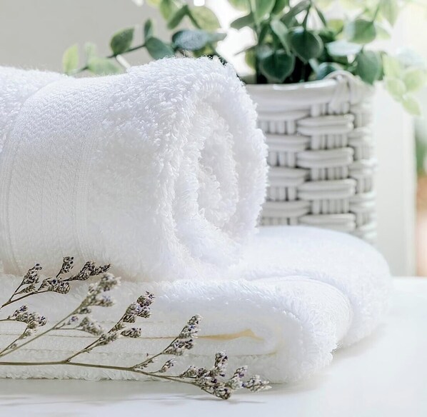 Una toalla blanca enrollada, una cesta tejida y flores de lavanda secas.