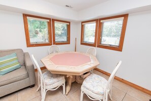 Ein Eckzimmer mit rundem Tisch, vier Stühlen, einer Couch und drei Fenstern mit Jalousien.