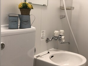 Ein Badezimmer mit Toilette, Bidet und Waschbecken. Auf dem Toilettentank befinden sich zwei Metallbehälter mit der Aufschrift 'GARDEN'.
