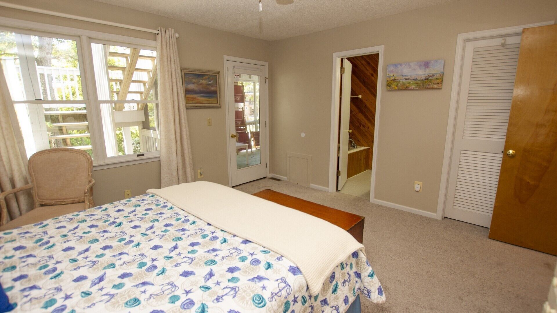 A bedroom with a bed, a chair, a door leading to a bathroom, and a painting on the wall.