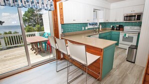 A kitchen with a view of the ocean, a dining area with chairs, and a small island with a sink.