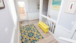 A hallway with a patterned rug, a yellow bench, and a painting of a beach scene. - Oceanside, Pool, Hot Tub, 945 ft to Beach Access, WW935, Sea Watch (Corolla)