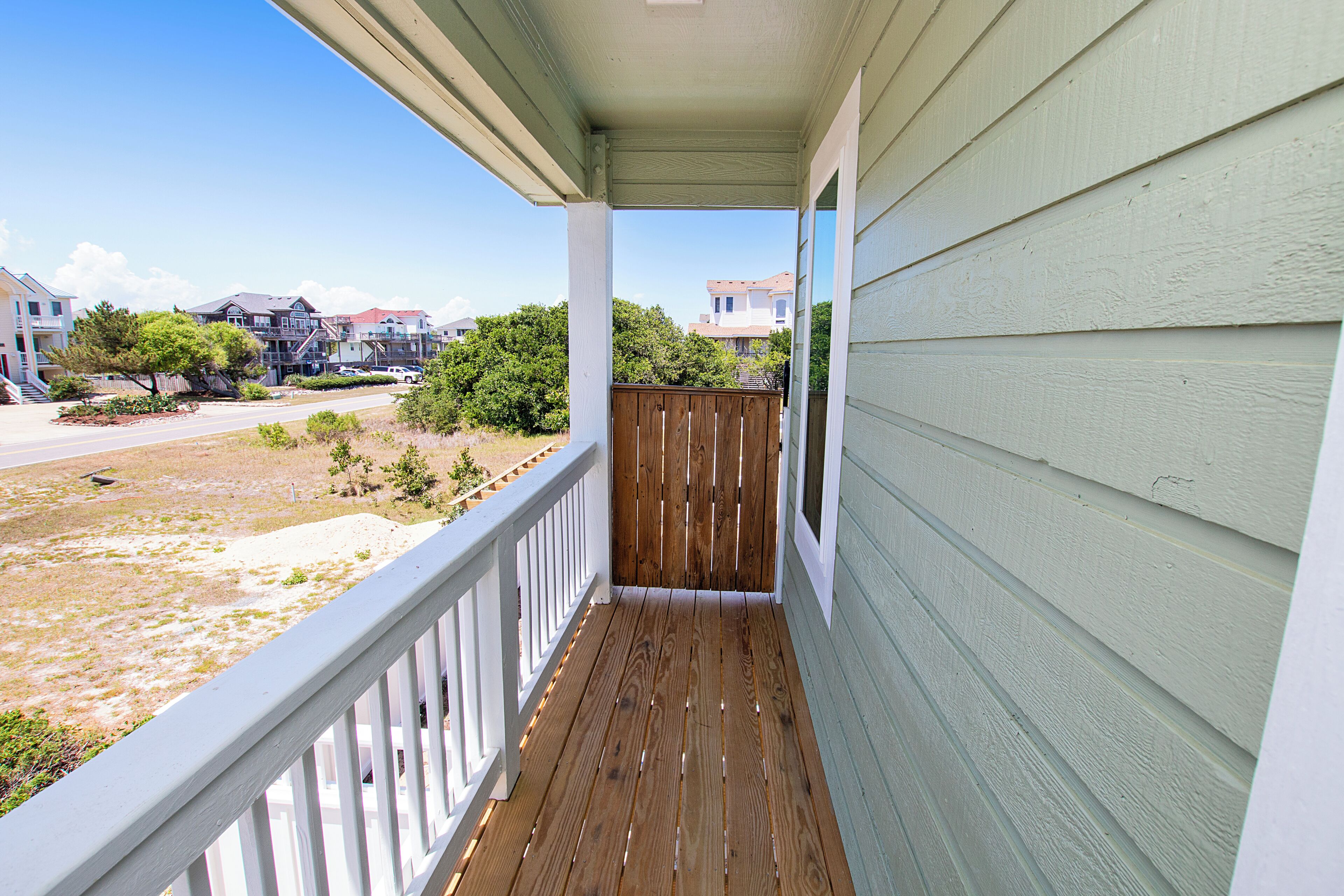A covered porch with a wooden railing, a view of a residential street, and houses in the background.