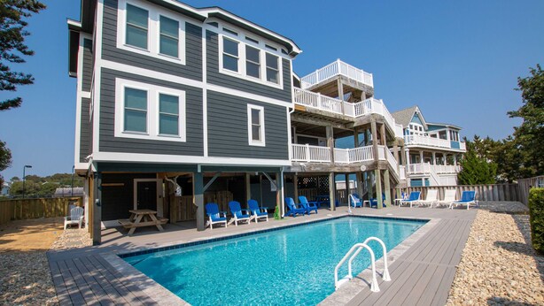 Ein zweistöckiges Haus mit Swimmingpool, Liegestühlen und einer überdachten Terrasse.