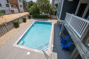 A rectangular swimming pool with a wooden deck and blue chairs on the right.