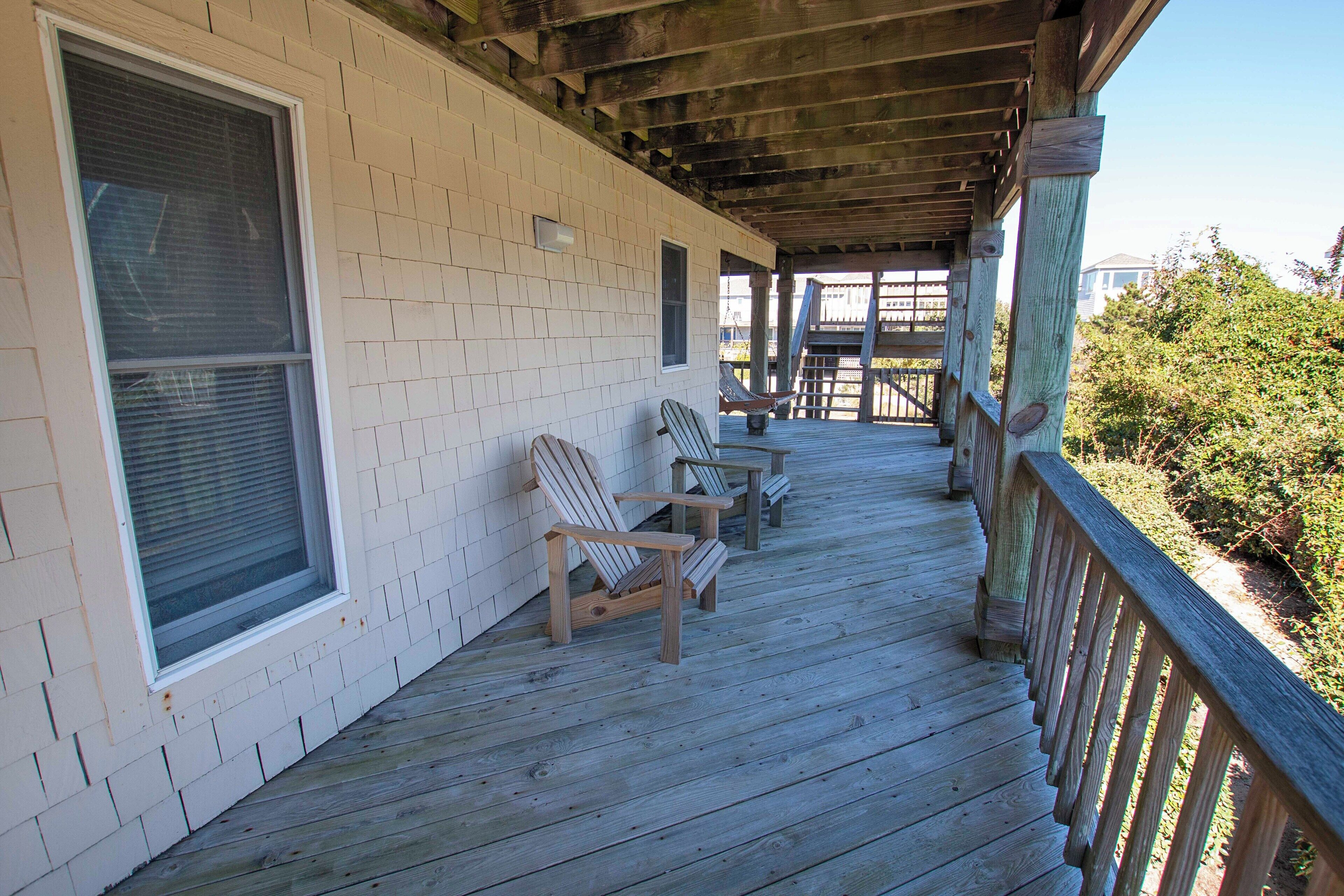 A covered porch with wooden chairs and a bench, a white brick wall, and a wooden railing.