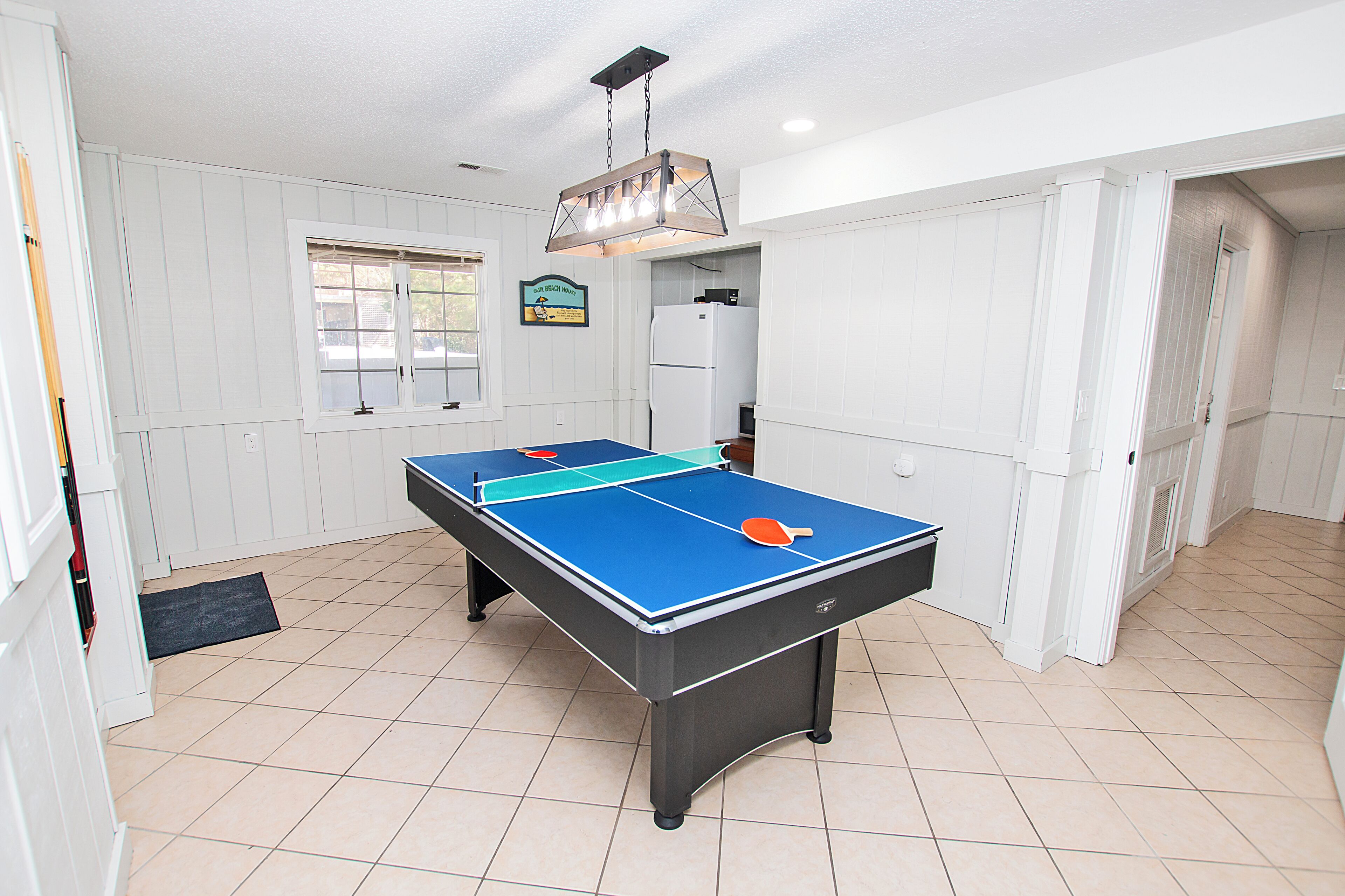 Una habitación con una mesa de ping pong, una puerta y una ventana.