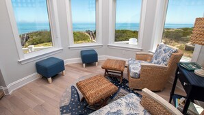 Ein sonnendurchflutetes Zimmer mit Meerblick, ausgestattet mit Korbmöbeln, einem gemusterten Teppich und Holzdielen.