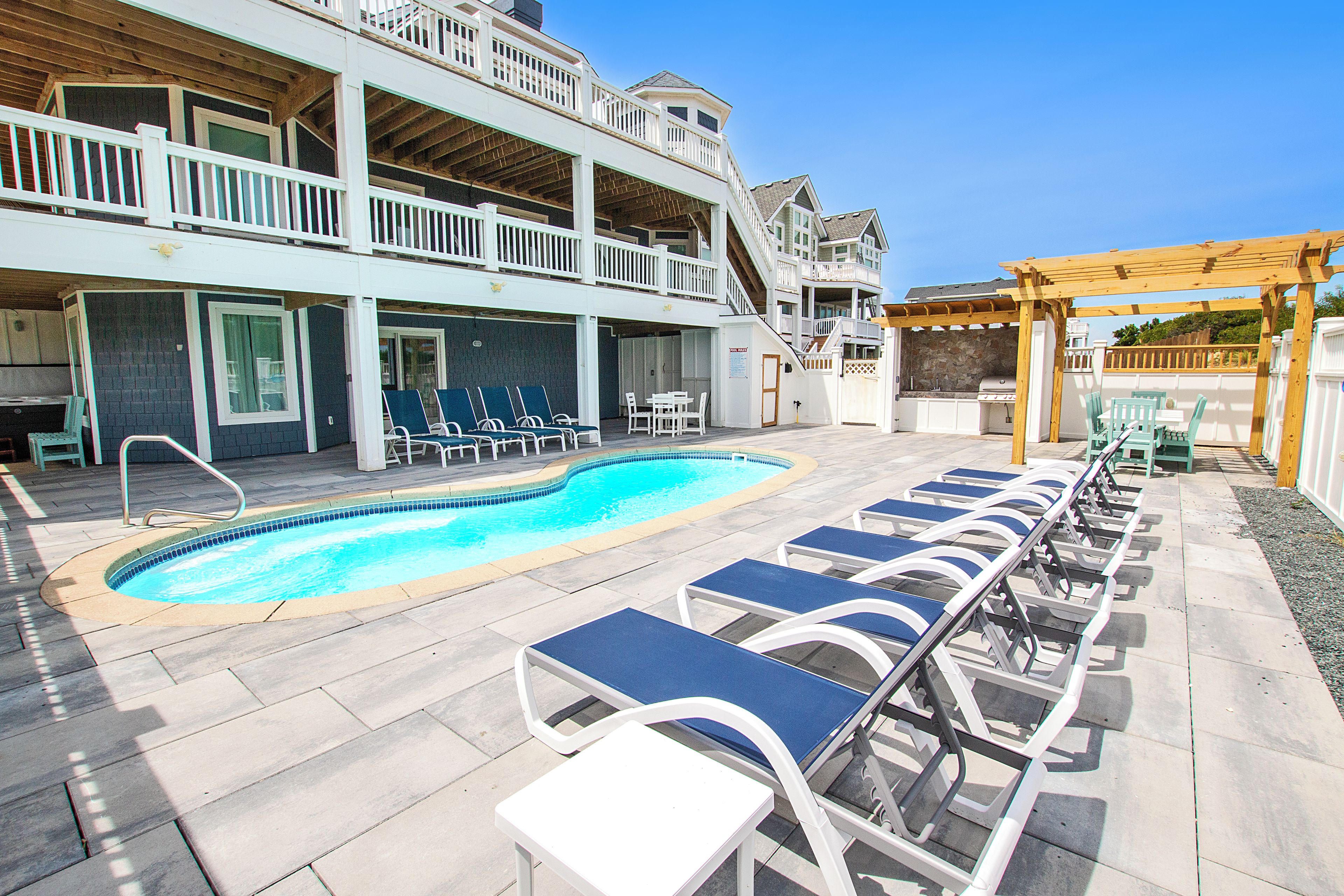 A poolside area with lounge chairs, a barbecue area, and a multi-level building with balconies.